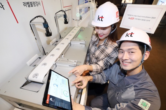 모델들이 KT 5G 스마트팩토리 상품을 보여주는 미니 제조 공정라인을 소개하고 있으며, 스마트패드를 통해 실시간으로 공장 내 상황을 확인할 수 있다.
