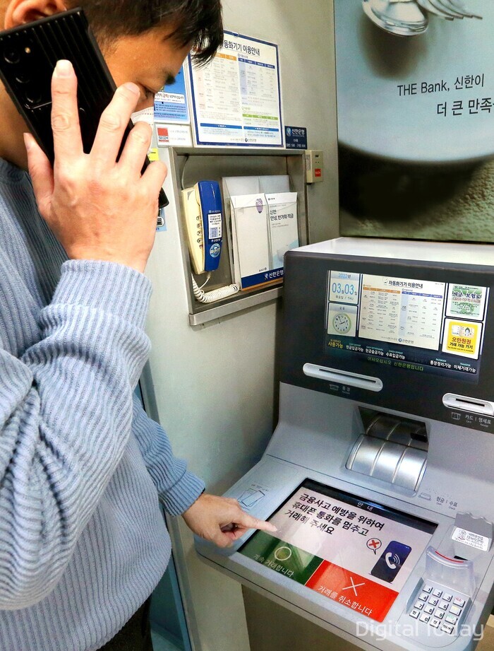 휴대폰 통화하며 신한은행 ‘AI 이상행동탐지 ATM’을 이용하고 있는 도중 ATM 화면에 금융사고 예방 주의 문구가 나오는 모습 [사진: 신한은행]