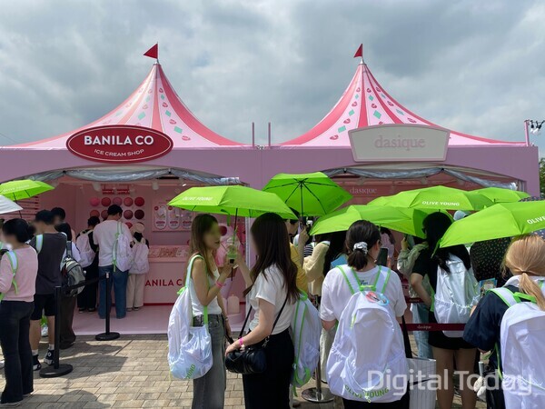 2025 올리브영 페스타에서 어드벤처 키트에 포함된 연두색 올리브영 양산을 쓰고 대기 중인 관람객들. [사진: 손슬기 기자]